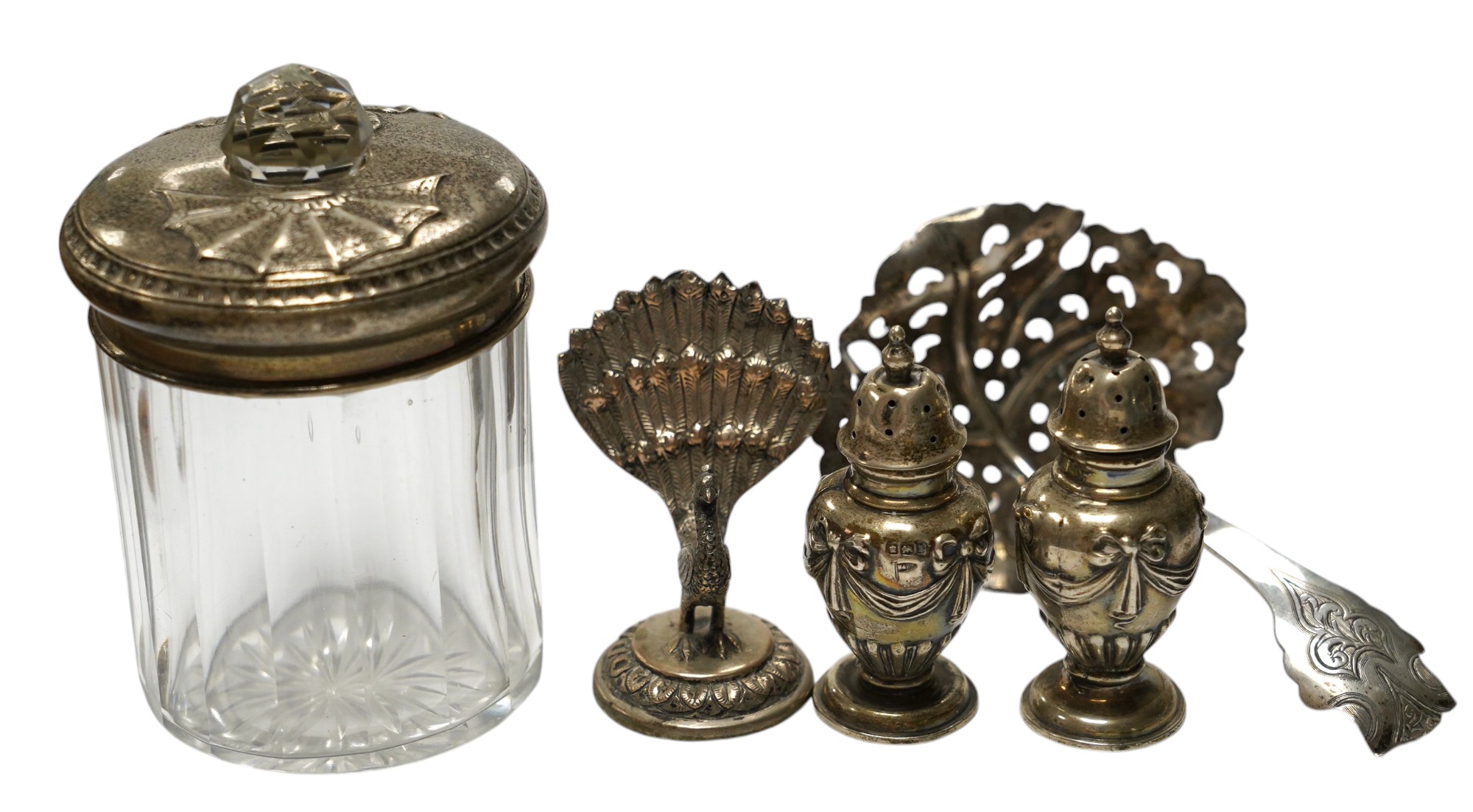 Three assorted modern silver wine labels, a ceramic wine label, a pair of silver pepperettes, a silver topped glass toilet jar, a Dutch white metal sifter spoon and seven plated items including a pair of peacock menu hol